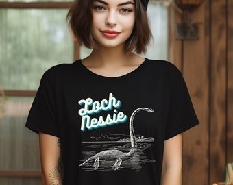 Może przedstawiać: Czarny T-shirt z retro grafiką potwora z Loch Ness i tekstem "Loch Nessie".