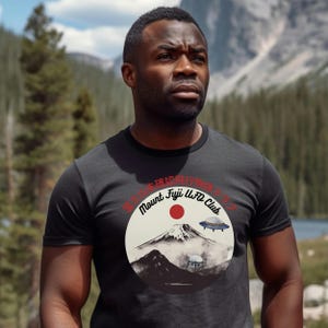 May include: A black t-shirt with a white circle graphic featuring a mountain, a red sun, and two flying saucers. The text "Mount Fuji UFO Club" is written in a red circle around the graphic. The Japanese text "富士山幽浮倶楽部" is written in a black circle around the graphic.