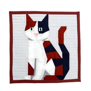 May include: A patchwork cat design in red, white, and navy blue. The cat is sitting upright, with a white body and patches of red and navy blue. The quilt is framed with a dark red border and a light grey background.