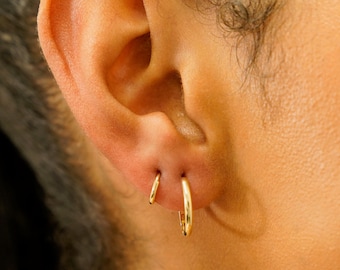 May include: A close-up of a person's ear with two gold hoop earrings. The larger hoop is in the lower lobe and the smaller hoop is in the upper lobe.