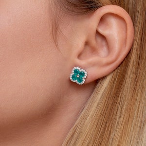 May include: A pair of silver earrings with a clover design. The clover is made of green gemstones surrounded by smaller clear gemstones.