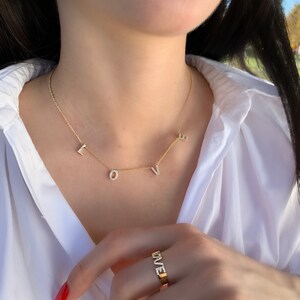 May include: A gold necklace with the word "LOVE" spelled out in diamonds. The necklace is worn by a person wearing a white shirt. The person is also wearing a gold ring with the word "LOVE" spelled out in diamonds.