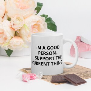 Könnte beinhalten: Eine weiße Keramiktasse mit schwarzem Text, der "Ich bin ein guter Mensch. Ich unterstütze das aktuelle Ding." lautet.