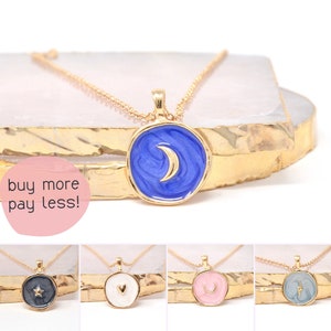 May include: Gold chain necklace with a round pendant featuring a blue enamel background with a gold crescent moon design.  Four other pendant designs are shown below: a black pendant with a gold star, a white pendant with a gold heart, a pink pendant with a gold crescent moon, and a blue pendant with a gold lightning bolt.