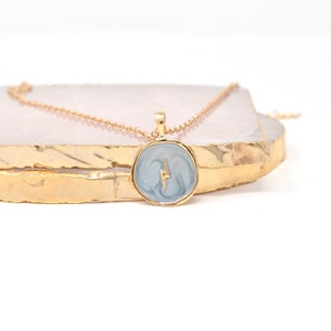 May include: A gold chain necklace with a round pendant featuring a light blue marbled design and a gold lightning bolt.