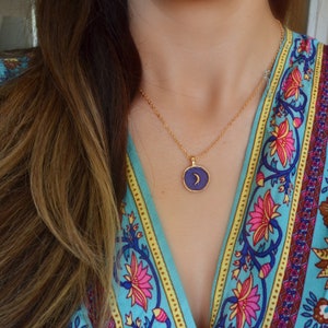 May include: A gold chain necklace with a purple pendant featuring a crescent moon design.
