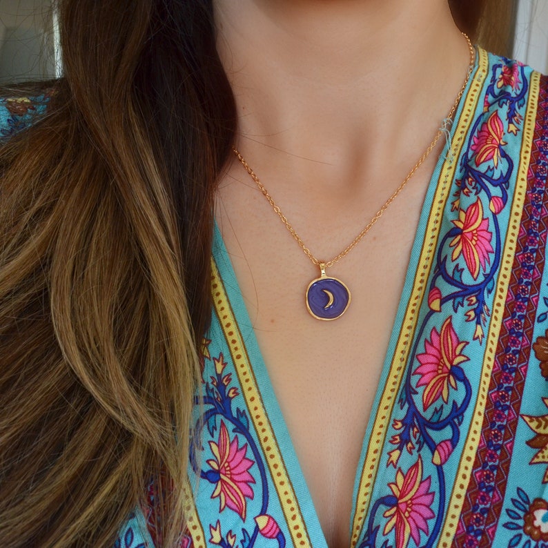 May include: A gold chain necklace with a purple pendant featuring a crescent moon design.