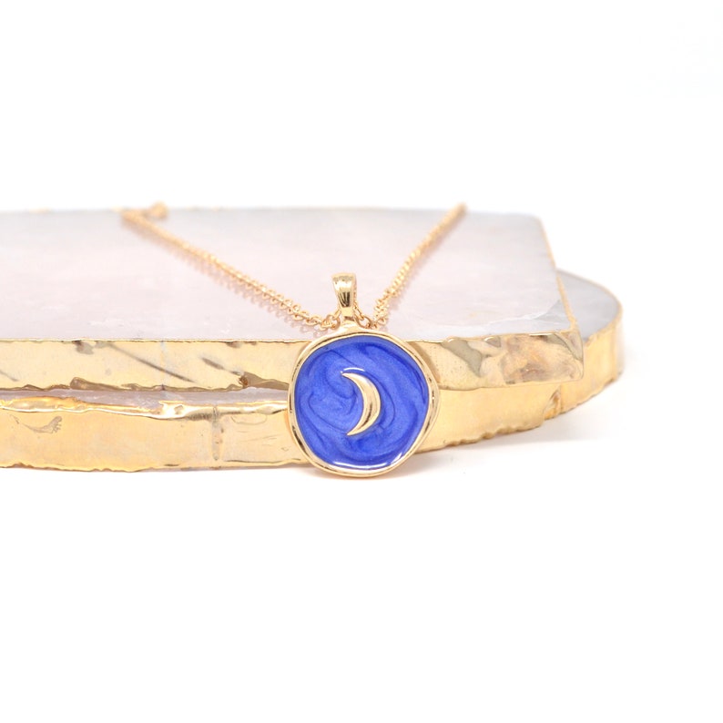 May include: Gold chain necklace with a blue enamel pendant featuring a crescent moon design.