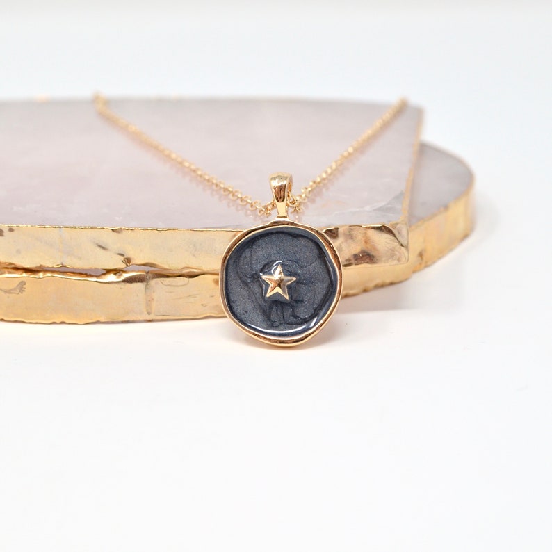 May include: A gold chain necklace with a dark gray pendant featuring a gold star in the center.