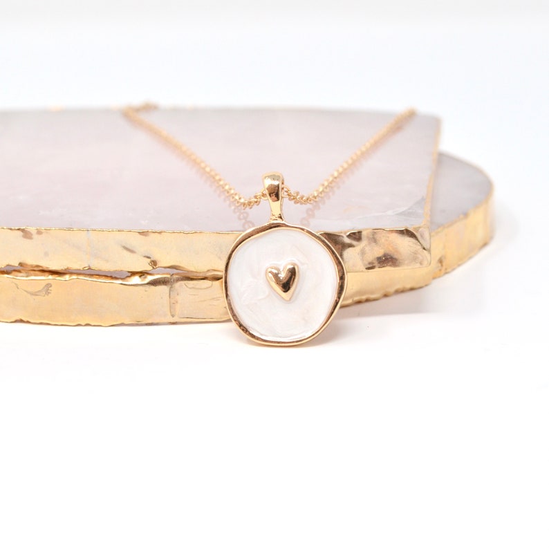 May include: A gold necklace with a white round pendant featuring a small gold heart in the center.