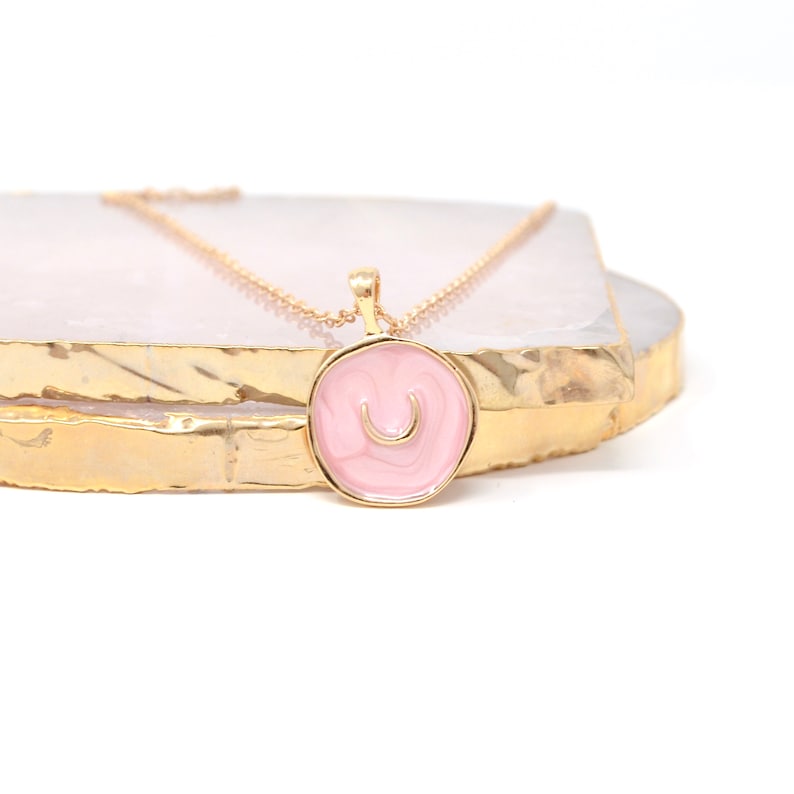 May include: A gold chain necklace with a pink enamel pendant featuring the letter "U" in a gold finish.
