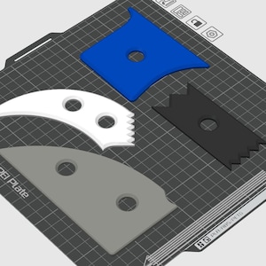Può includere: Quattro strumenti di stampa 3D in plastica blu, bianca, grigia e nera. Gli strumenti hanno varie forme, tra cui un raschietto curvo, un bordo dentellato e un bordo piatto. Gli strumenti sono su una superficie a griglia nera.
