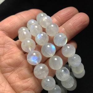 May include: A stack of three bracelets made of white moonstone beads. The beads are round and have a slight iridescent sheen.