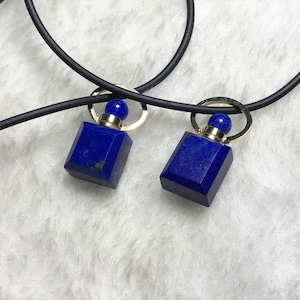 May include: A black cord necklace with two square lapis lazuli pendant charms. Each charm has a gold top with a small round blue stone.