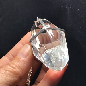 May include: A clear quartz crystal pendant with a silver cage setting. The pendant is hanging from a silver chain.