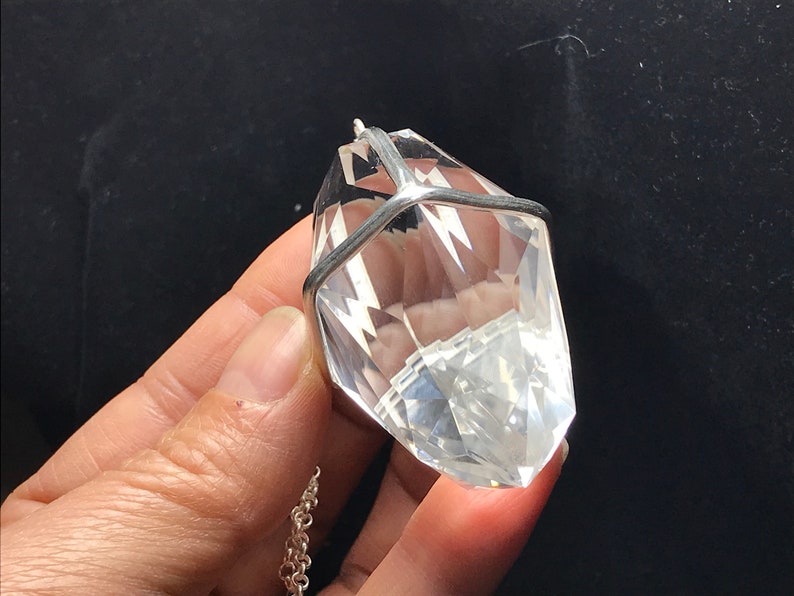 May include: A clear quartz crystal pendant with a silver cage setting. The pendant is hanging from a silver chain.