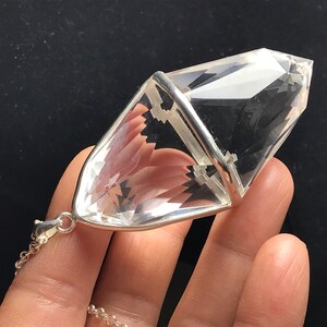 May include: A clear quartz crystal pendant with a silver setting. The crystal is shaped like a double-pointed pyramid and is attached to a silver chain.