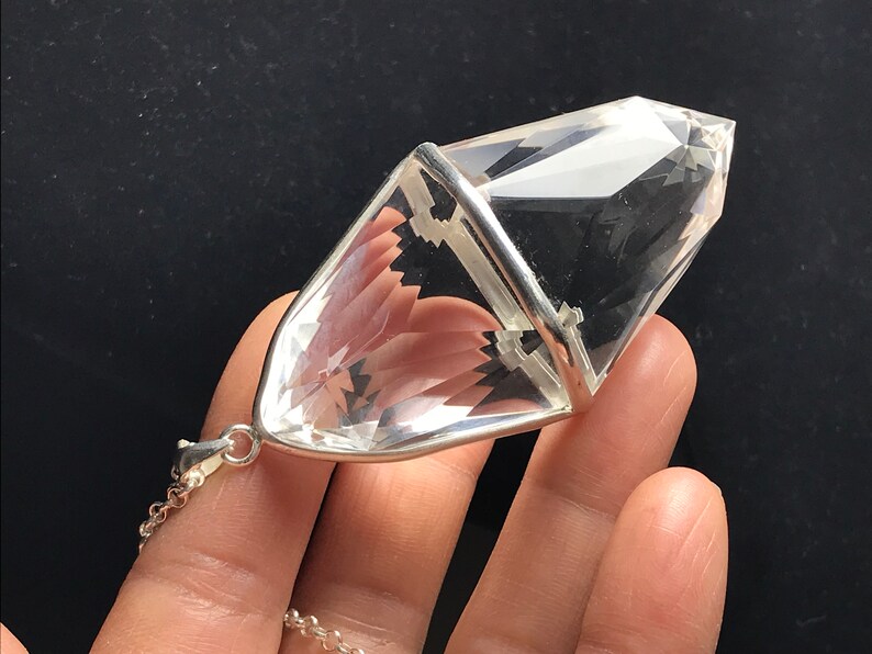 May include: A clear quartz crystal pendant with a silver setting. The crystal is shaped like a double-pointed pyramid and is attached to a silver chain.