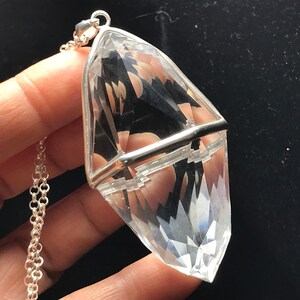 May include: A clear quartz crystal pendant with a silver setting. The crystal is faceted and has a pointed tip. The pendant is attached to a silver chain.