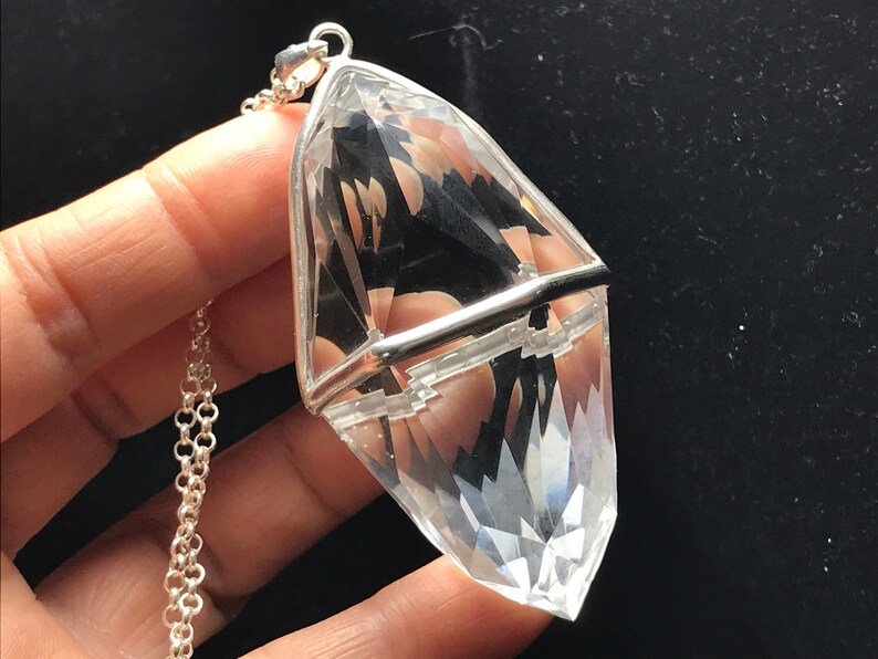 May include: A clear quartz crystal pendant with a silver setting. The crystal is faceted and has a pointed tip. The pendant is attached to a silver chain.