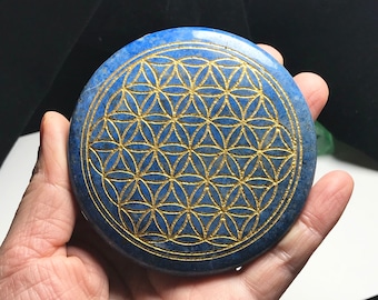 May include: A round, blue lapis lazuli stone with a gold-colored flower of life design etched into the surface.