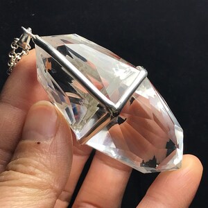 May include: A clear quartz crystal pendant with a silver setting. The crystal is faceted and has a pointed tip. The pendant is attached to a silver chain.
