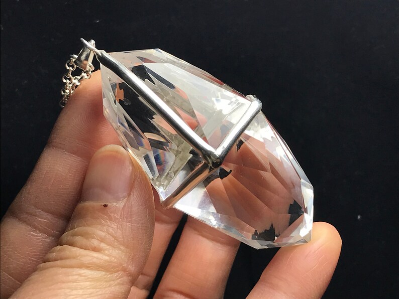 May include: A clear quartz crystal pendant with a silver setting. The crystal is faceted and has a pointed tip. The pendant is attached to a silver chain.