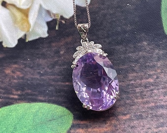 May include: A silver pendant necklace with a large oval amethyst gemstone surrounded by smaller clear gemstones. The pendant is on a silver chain.