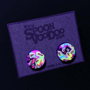 May include: A pair of iridescent round stud earrings with a swirling pattern. The earrings are on a purple card with the text "www.spoonvoodoo.com".