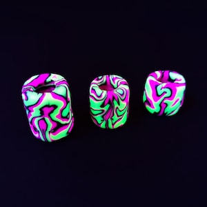 Könnte beinhalten: Drei kleine, zylindrische, neon-grüne, rosa und schwarze Keramikperlen mit einem Wirbelmuster.