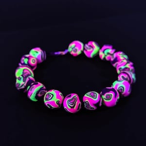 May include: A necklace made of pink, green, and black marbled beads. The beads are round and have a swirling pattern.