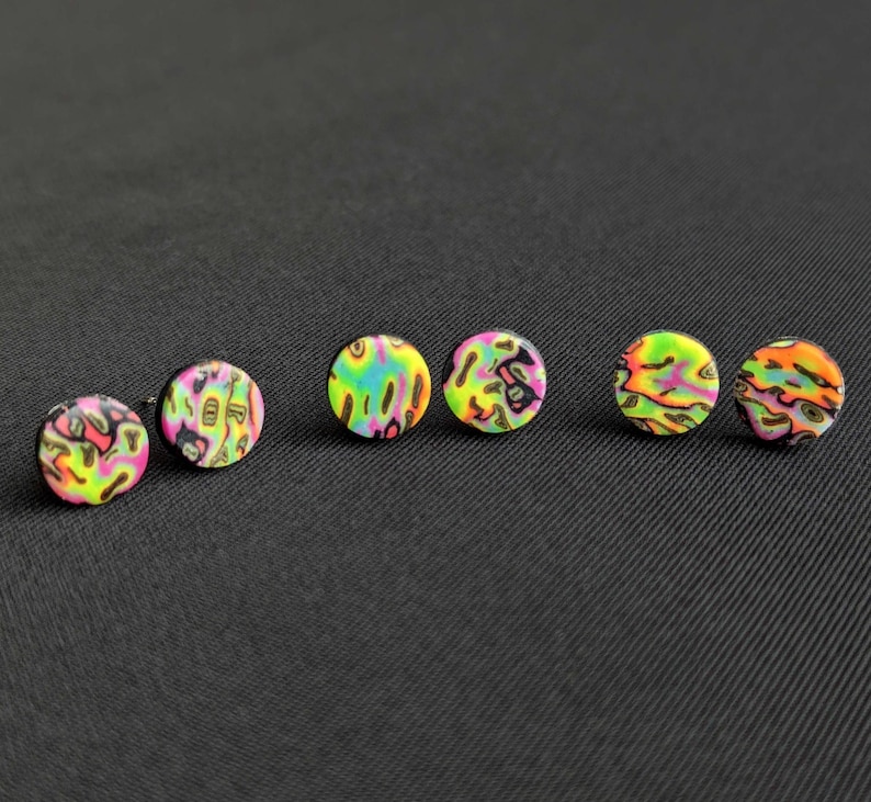 May include: Five colourful round earrings with a black background. The earrings have a psychedelic pattern with pink, green, yellow, and black colours.