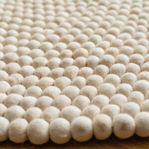 Op de afbeelding: Close-up van een wit, pluche vloerkleed gemaakt van kleine, ronde wollen ballen.