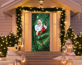 May include: A Christmas-themed door cover featuring Santa Claus in a red suit and white beard, emerging from a green sack. The door is decorated with a garland of lights and is surrounded by lit lanterns and small Christmas trees, creating a festive holiday scene.