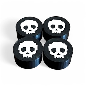 Könnte beinhalten: Vier schwarze runde knopfartige Schädel mit einem weißen pixelartigen Schädel-Design.