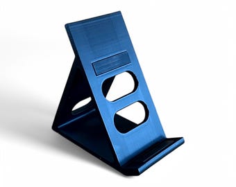 May include: A black plastic phone stand with two cutouts for holding a phone in portrait or landscape mode.