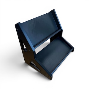 Puede incluir: Un soporte de exhibición de dos niveles en color negro mate con un diseño escalonado que incluye dos estantes planos. Los paneles laterales tienen recortes triangulares y están fijados con tornillos visibles. La estructura está inclinada.