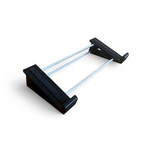 May include: A black, rectangular stand with two angled supports and two silver rods. The stand is designed to hold an item, with a flat surface on each end. The item is set against a white background.