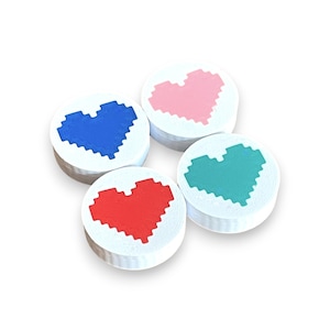 May include: Four white, round objects with pixelated heart designs in blue, pink, red, and teal. The hearts are centered on the objects, which are stacked in a slightly offset arrangement against a white background.