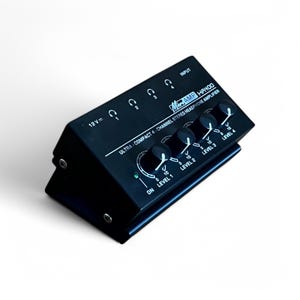 Può includere: Amplificatore per cuffie stereo a 4 canali nero con manopole del volume individuali per ogni canale. Il dispositivo è etichettato "Mini Amp Hayoo" e "Amplificatore per cuffie stereo a 4 canali ultracompatto".