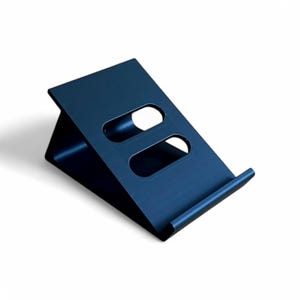 May include: A dark blue metal phone stand with two cutouts for charging cables. The stand is angled to hold a phone upright.