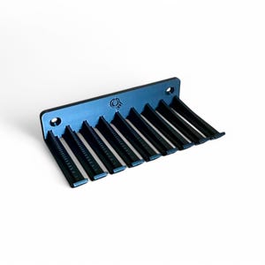 Puede incluir: Un soporte de peines de pared negro con diez ranuras para peines. El soporte tiene un pequeño logotipo en la parte delantera.