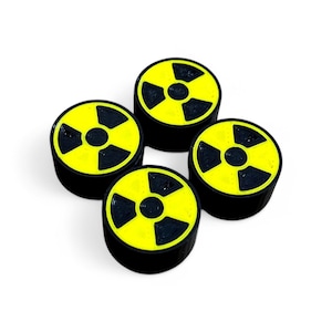 Puede incluir: Cuatro botones redondos negros y amarillos con un símbolo de radiación impreso en ellos.