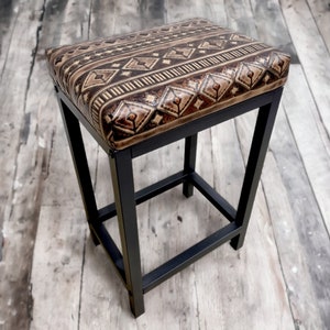 May include: A black metal bar stool with a brown leather seat featuring a geometric pattern.