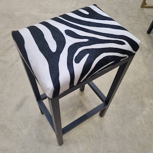 Könnte beinhalten: Ein schwarzer Barhocker aus Metall mit einem Sitz aus Zebra-Muster.