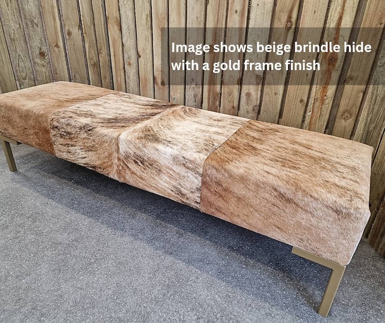 May include: Beige and brown cowhide bench with a gold metal frame. The bench is made of three sections and has a rectangular shape.