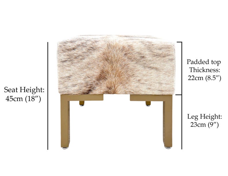 May include: A square ottoman with a cowhide top in shades of brown and cream, supported by gold-colored metal legs. The seat height is 18 inches, the padded top is 8.5 inches thick, and the leg height is 9 inches.