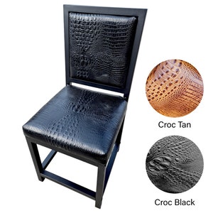 May include: Black metal chair with a black crocodile-embossed leather seat and back. The chair has a square back and a square seat. The chair is on a white background. Two close-up images of the leather are shown below the chair. The first image is of tan crocodile-embossed leather with the text "Croc Tan" below it. The second image is of black crocodile-embossed leather with the text "Croc Black" below it.