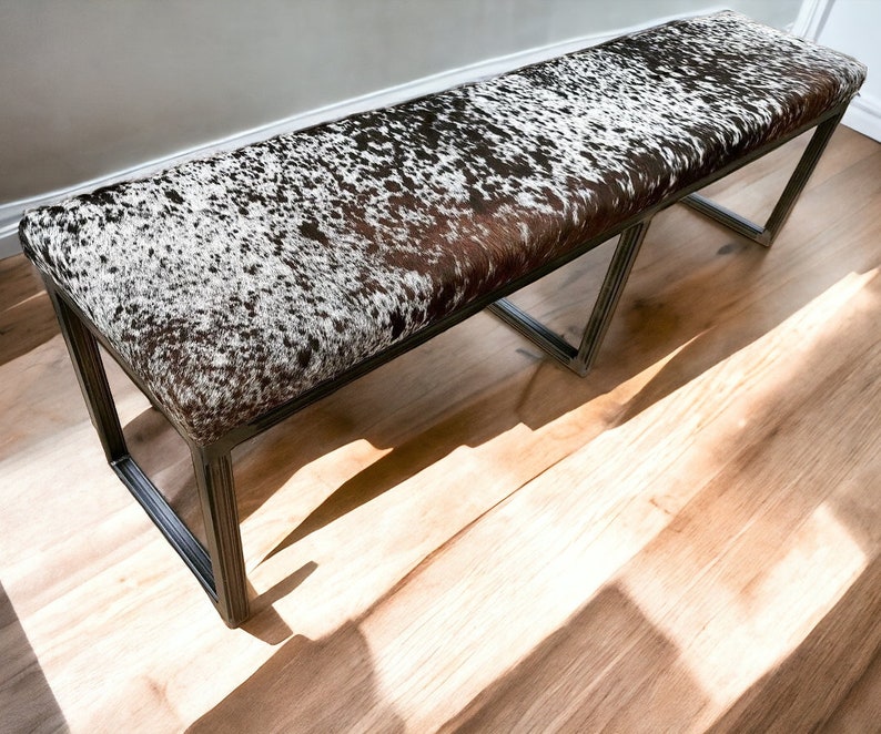 May include: A long, rectangular bench with a black metal frame and a brown and white cowhide seat.