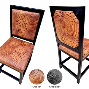 May include: Two black metal dining chairs with a crocodile embossed brown leather seat and back. The chairs have a square back and a simple design.